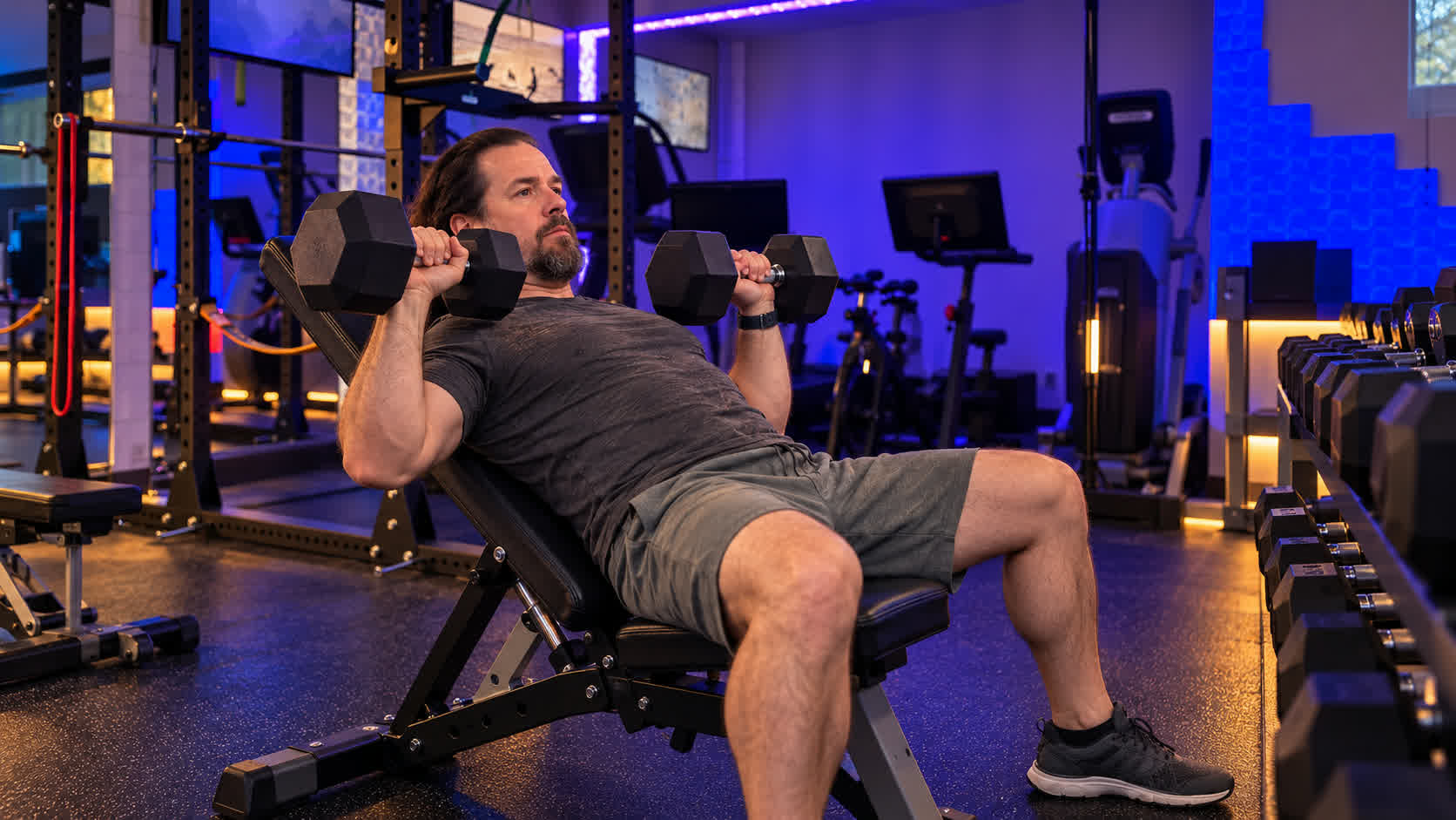 Illustration of Keith holding dumbbells on an incline bench in his gym.